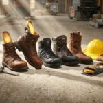 Lineup of work boots on a jobsite with a visible removable insole showing arch support beside a hard hat and safety vest