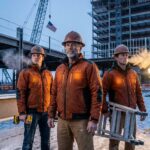 Construction workers on a winter jobsite wearing high-visibility heated jackets with hard hats and tools